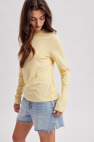 woman wearing a yellow and white striped long sleeve top with a slight mock neck and paired with a denim mini skirt