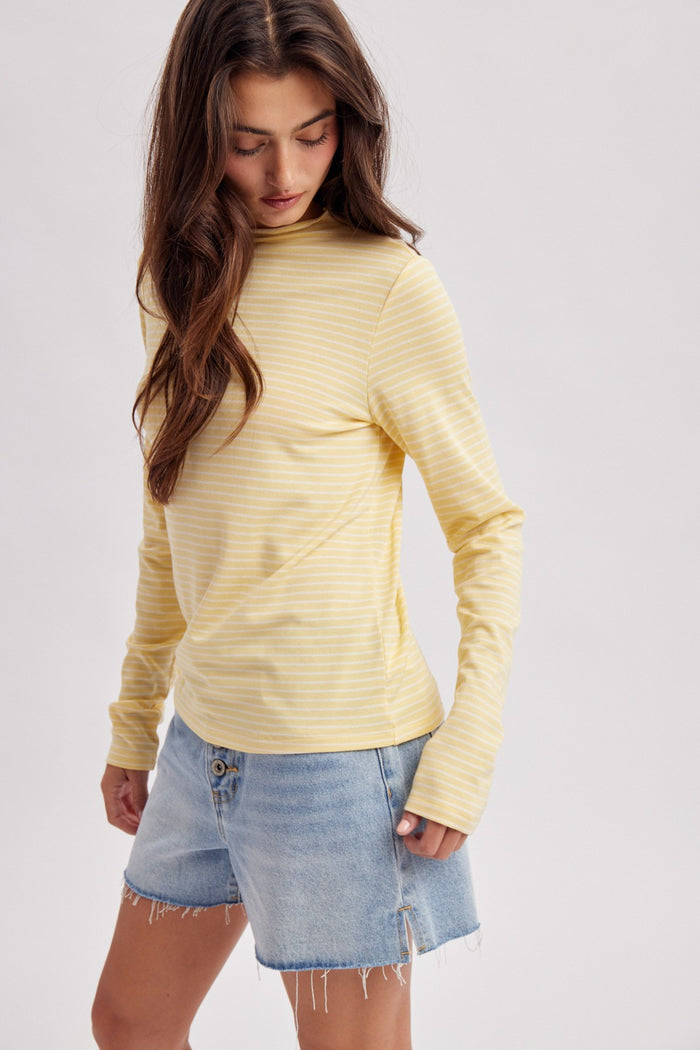 woman wearing a yellow and white striped long sleeve top with a slight mock neck and paired with a denim mini skirt