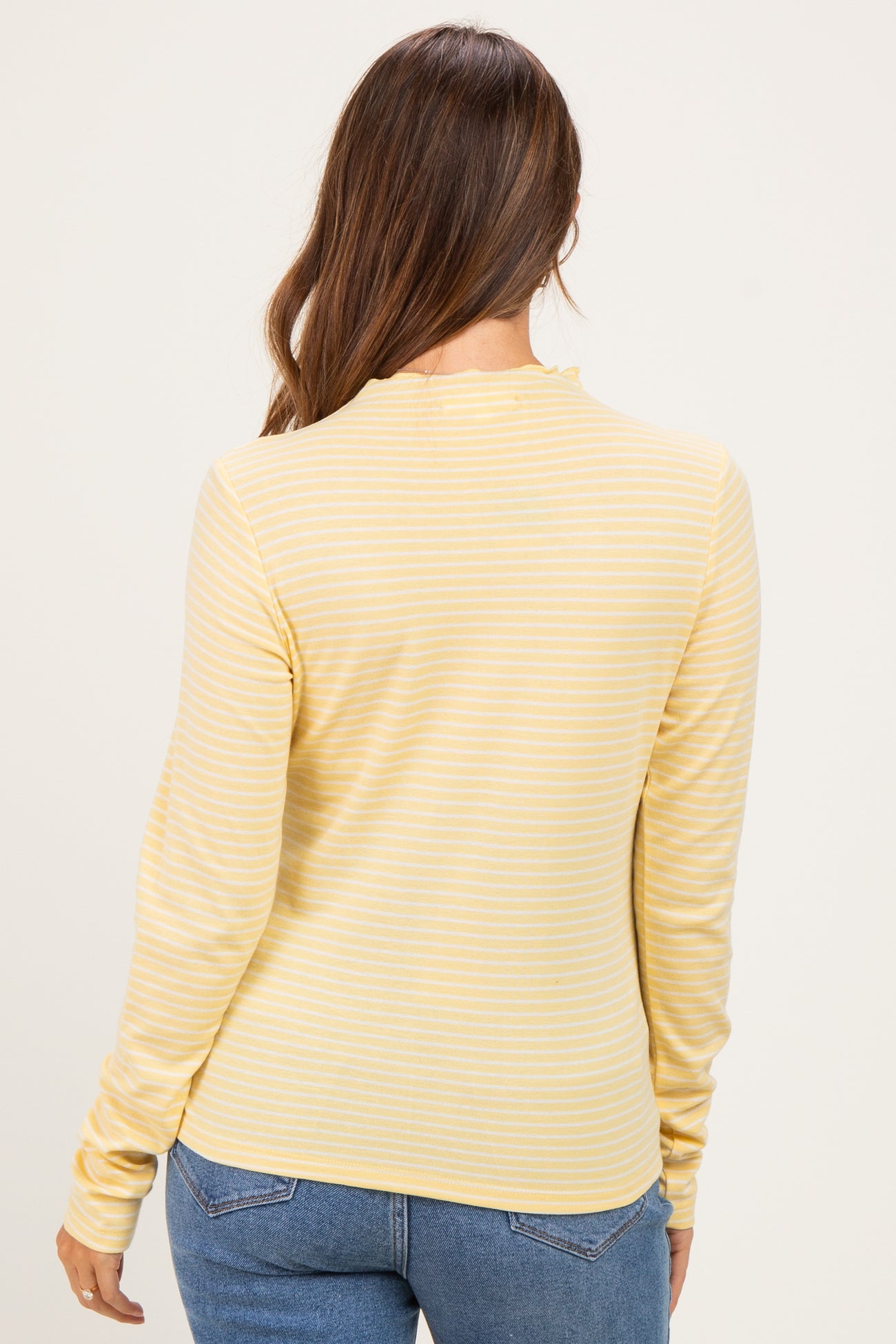 woman wearing a yellow striped long sleeve maternity top, viewed from the back, paired with blue jeans