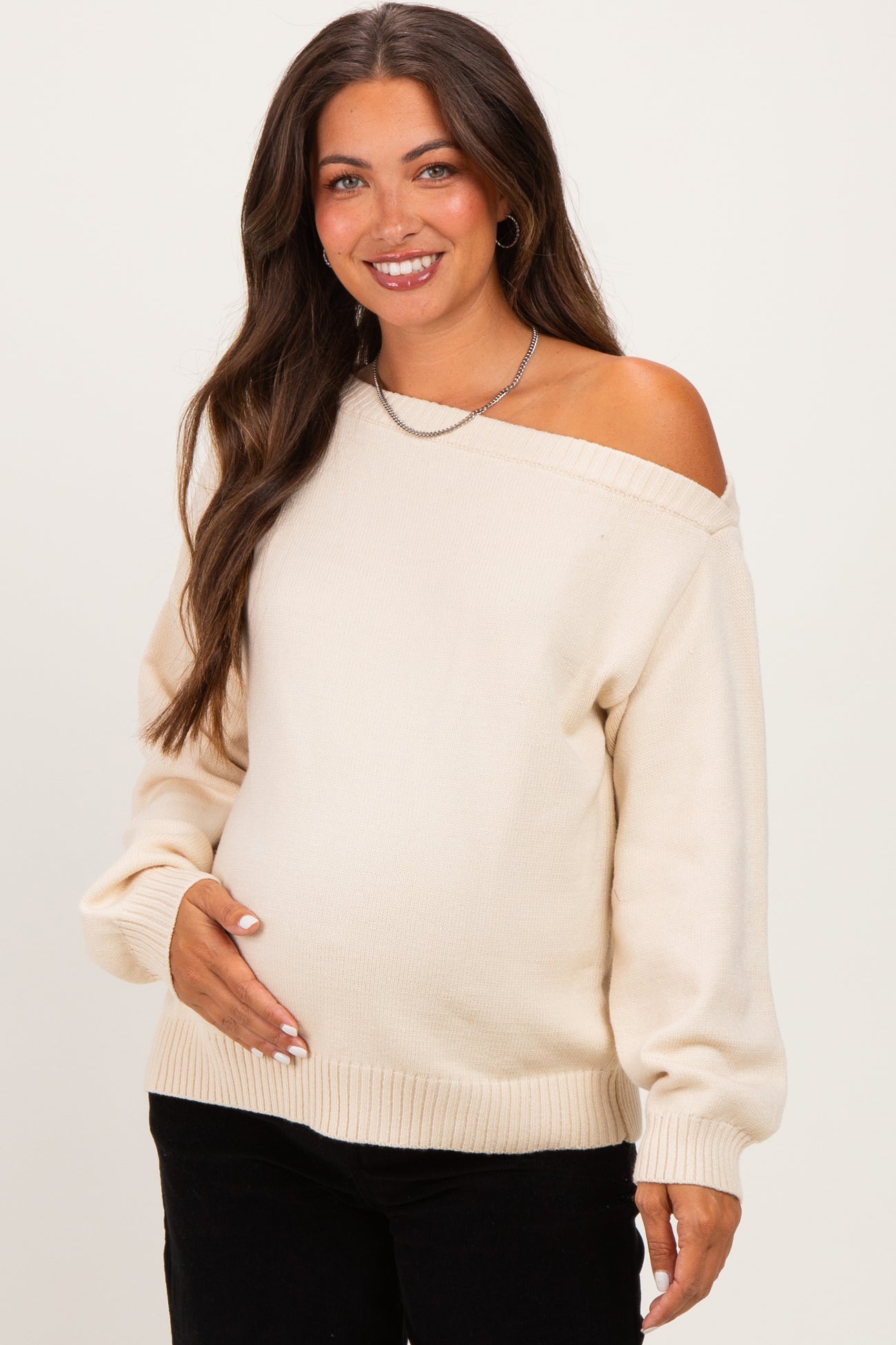 woman wearing a cream off-the-shoulder maternity sweater and holding her baby bump