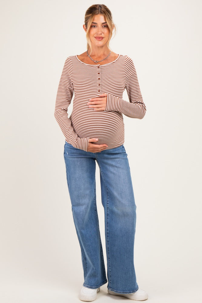 woman wearing a rust and cream striped maternity top and blue flared jeans, holding her baby bump