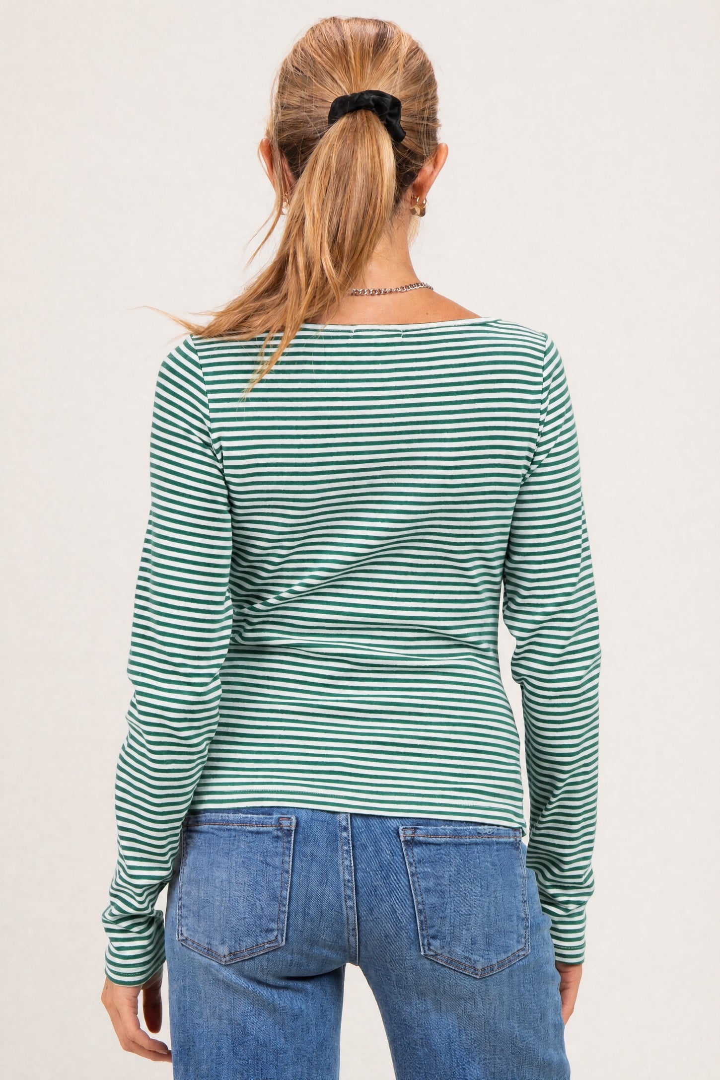 woman wearing a green and white striped long sleeve maternity top, shown from the back with light blue jeans