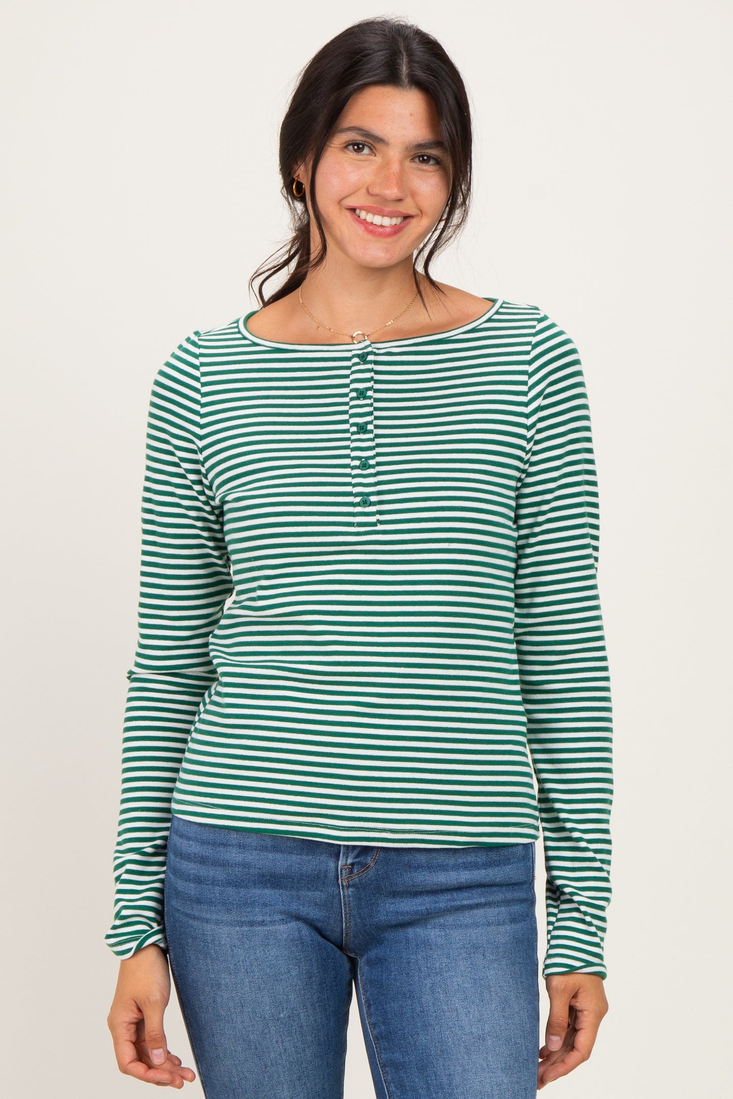 woman wearing a green and white striped long sleeve henley top with buttons and blue jeans