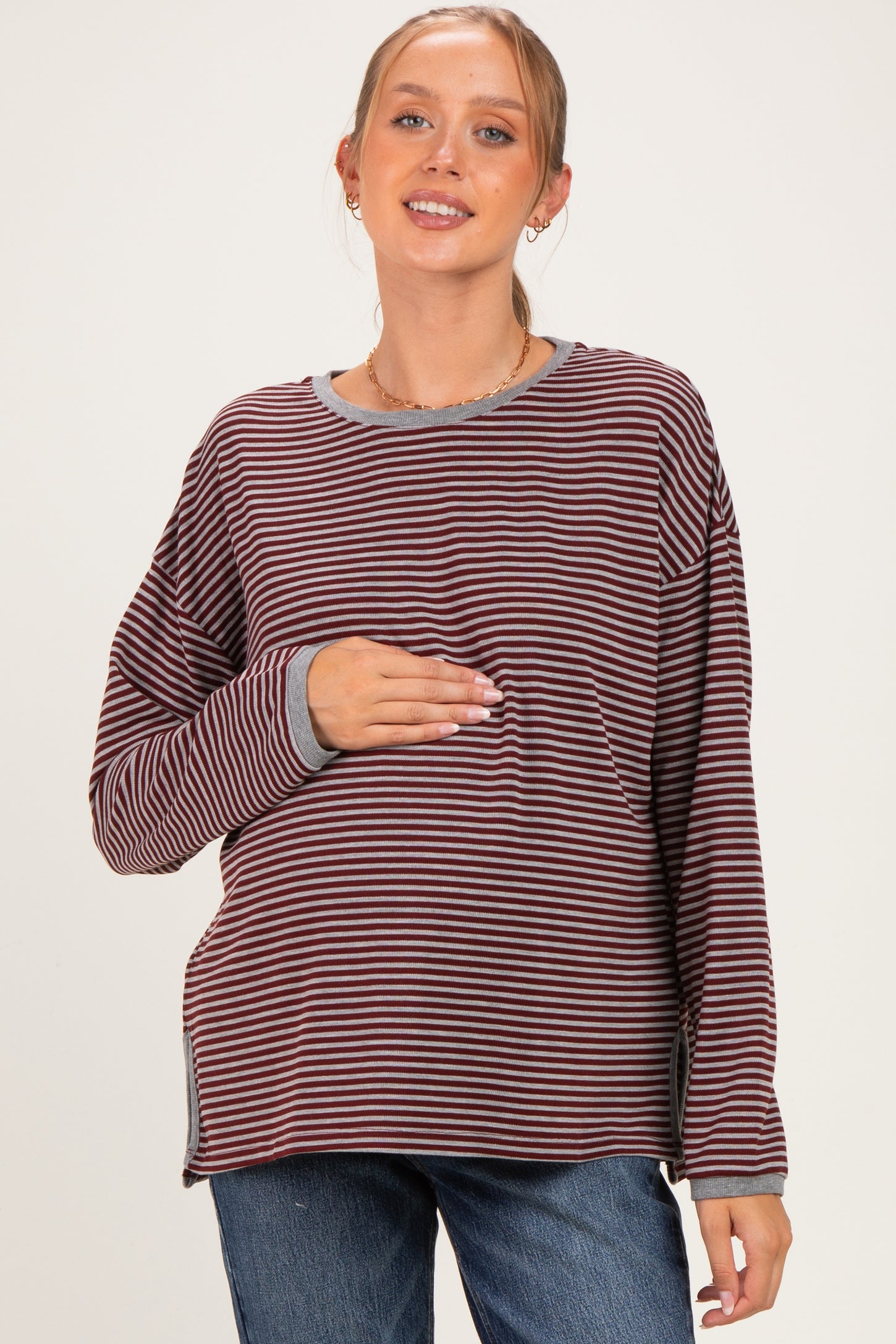 woman wearing a striped long sleeve maternity top and holding her baby bump