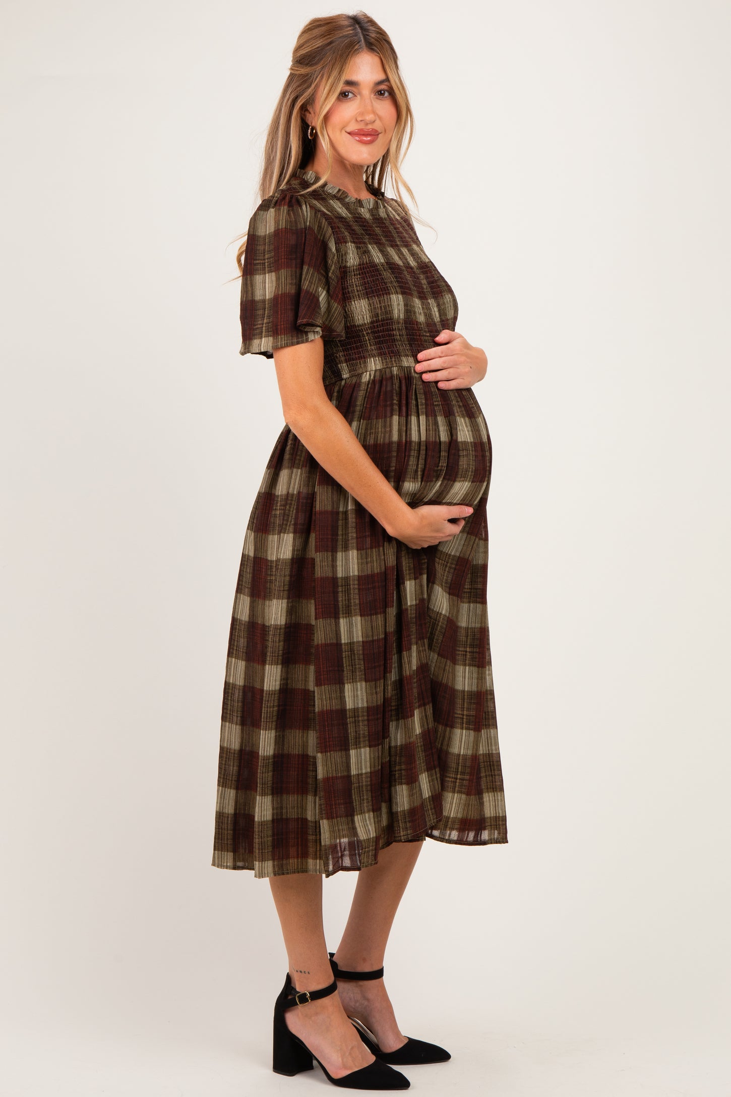 woman wearing a brown and olive green plaid maternity dress and holding her baby bump