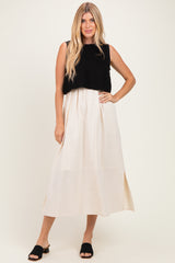 woman wearing a black knitted crop top over a cream maxi dress with side slits and black slide sandals