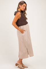 woman wearing a brown knitted maternity crop top and a beige maxi dress with side pockets and a front slit, showing her baby bump