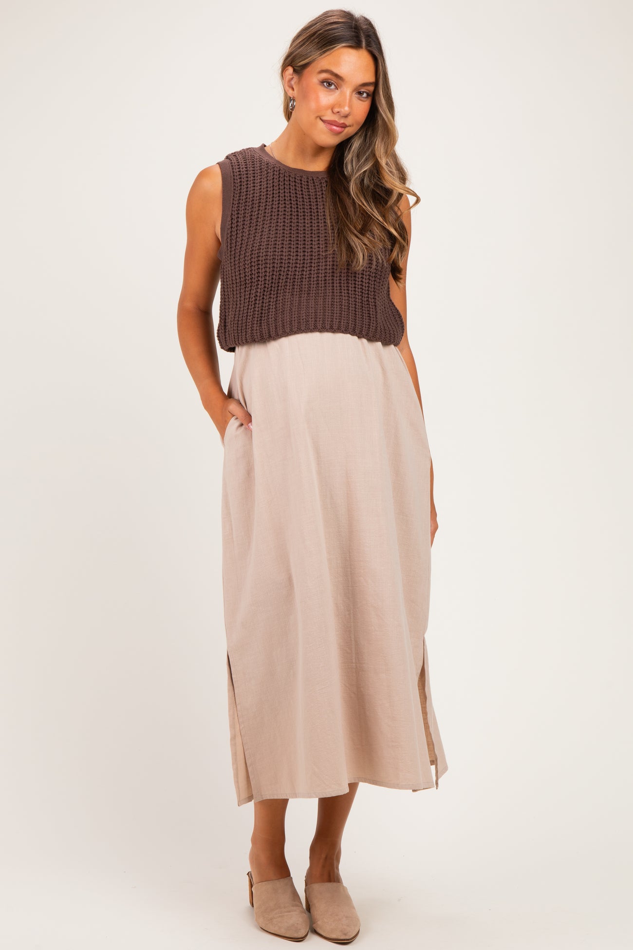 woman wearing a brown knitted maternity top over a beige maxi dress with side slits and pockets, showing a baby bump