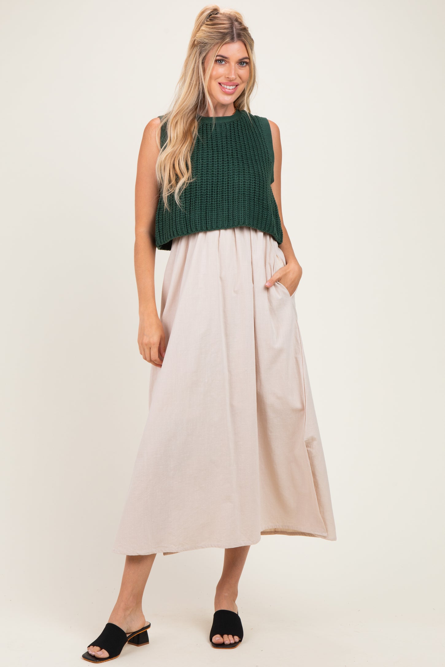 woman wearing a dark green knitted cropped sweater over a light beige maxi dress with pockets