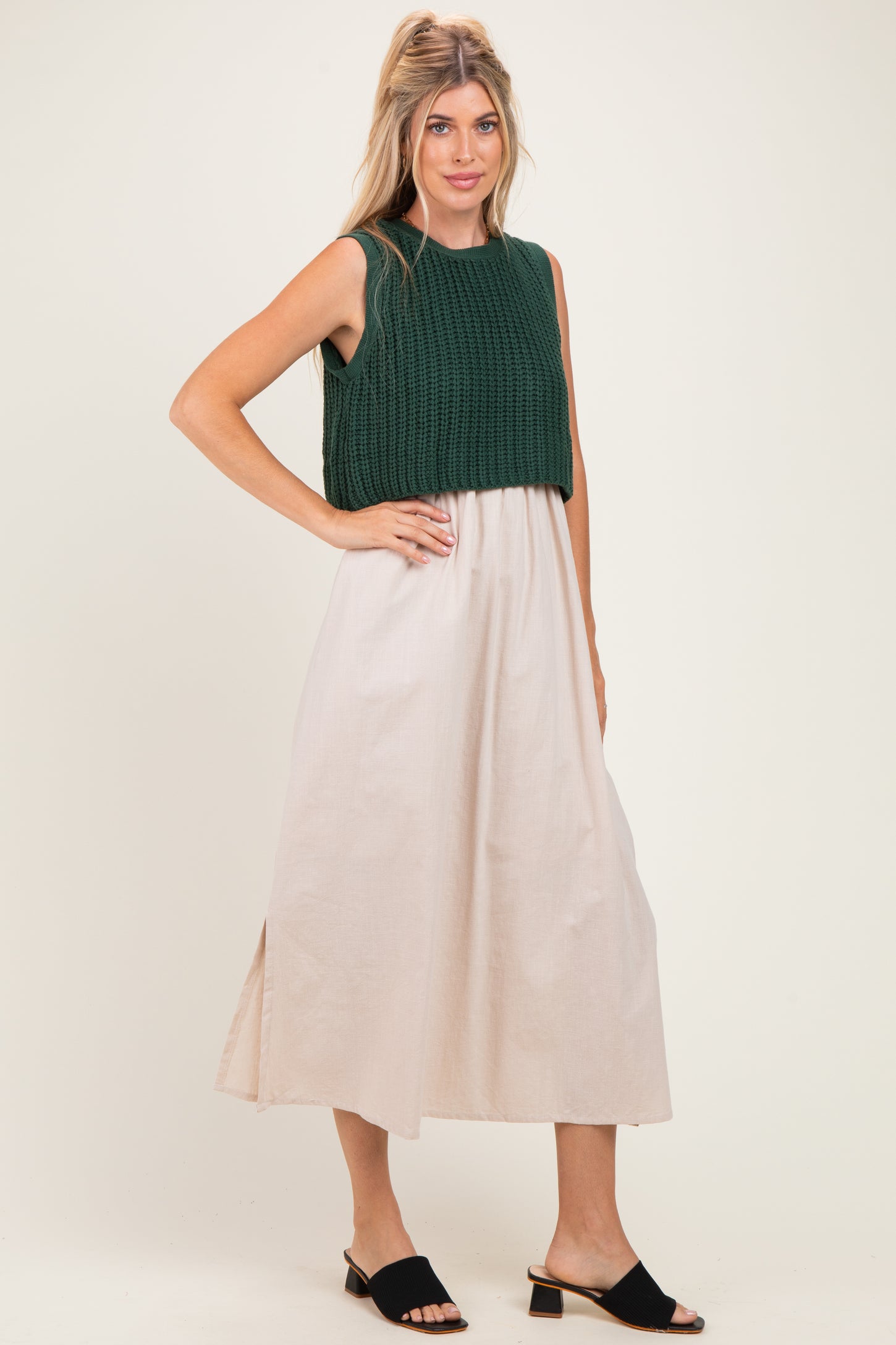 woman wearing a dark green knitted crop top and a light beige maxi skirt, standing in open-toe black mules