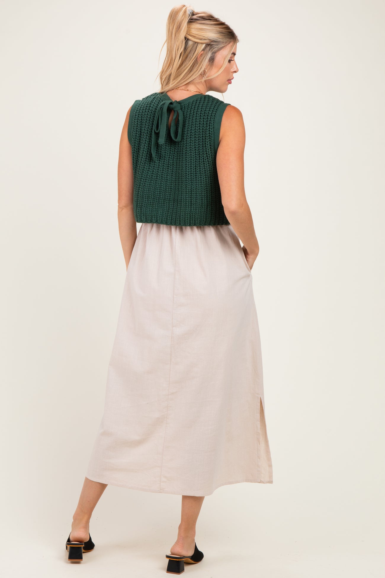 woman wearing a green knitted cropped top over a beige maxi dress with side pockets and a slit detail