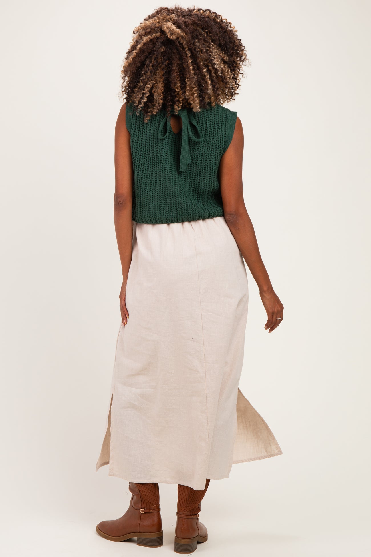 woman wearing a green knitted sleeveless top and a long beige skirt, showing a baby bump from behind