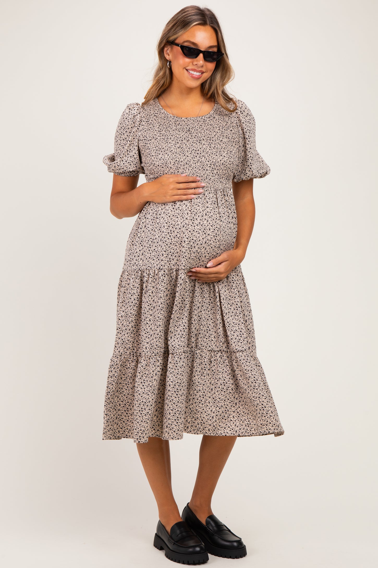 woman wearing a floral print maternity dress with puff sleeves and a tiered skirt, holding her baby bump