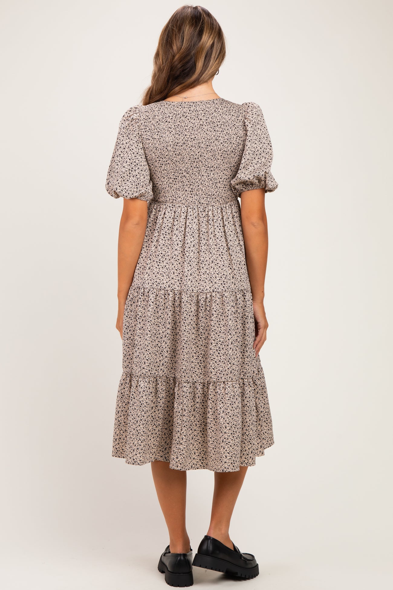 woman wearing a floral print maternity dress with puff sleeves and a tiered skirt, showing a baby bump from the back