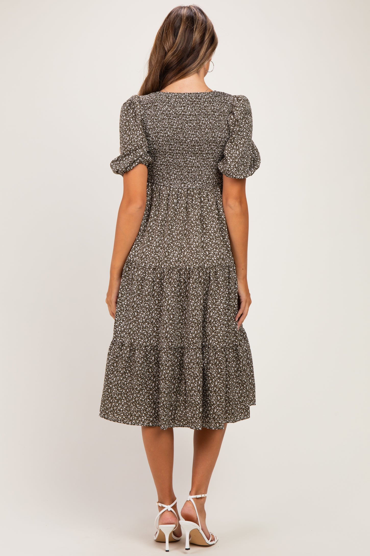 woman wearing a dark floral print maternity dress with puff sleeves and a tiered skirt, showing a baby bump from the back