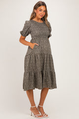woman wearing a dark floral print maternity dress with puff sleeves and pockets, showing her baby bump