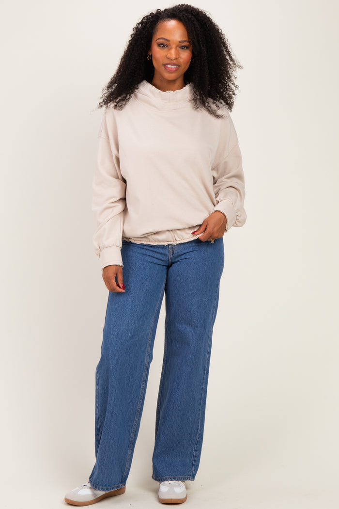 woman wearing a beige pullover sweatshirt with a ruffled collar and wide-leg blue jeans