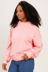 woman wearing a pink long sleeve sweatshirt with a high neck and ruffled hem, styled with blue jeans