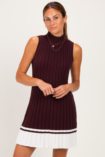 woman wearing a dark burgundy sleeveless ribbed knit dress with a pleated white hem and layered gold necklaces