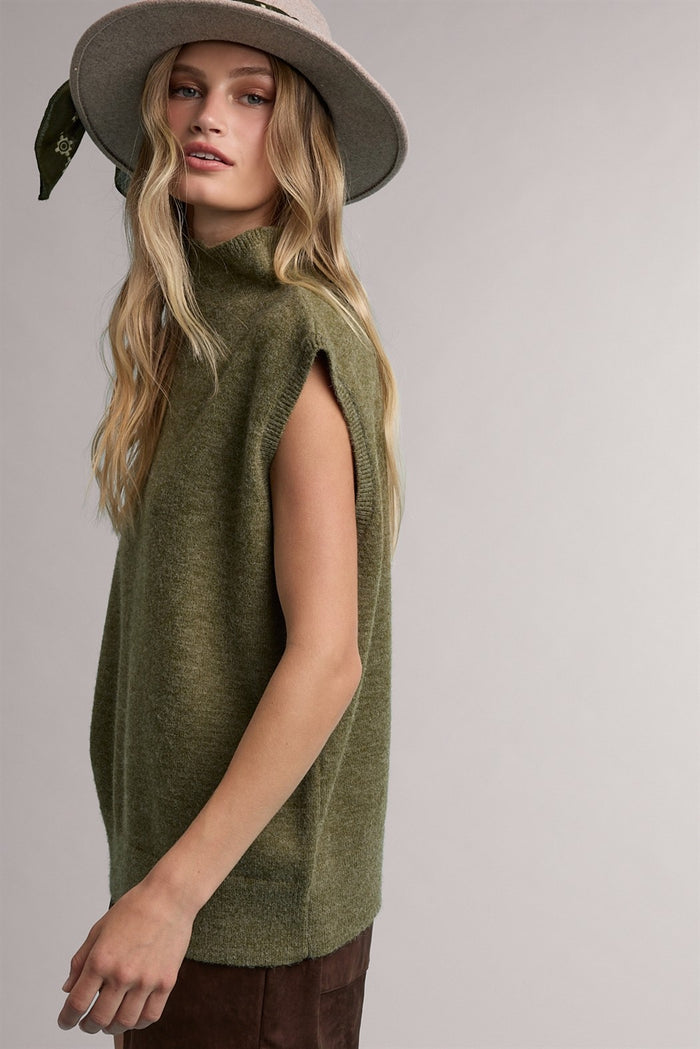 woman wearing a green sleeveless turtleneck sweater and a wide-brimmed hat