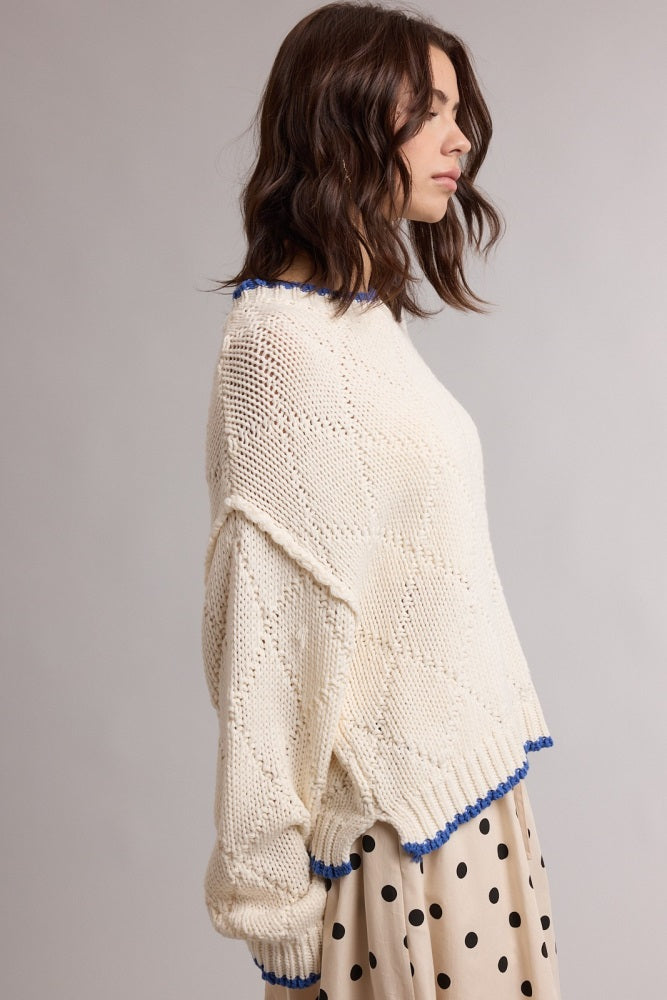 woman wearing a cream colored knitted sweater with blue trim and a loose fit, paired with a polka dot skirt