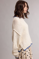 woman wearing a cream colored knitted sweater with blue trim and a loose fit, paired with a polka dot skirt