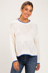woman wearing a white knit maternity sweater with blue trim and a relaxed fit, smiling at the camera