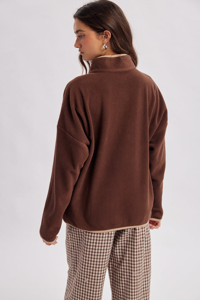 woman wearing a brown fleece pullover with a high collar and oversized fit, paired with checkered trousers