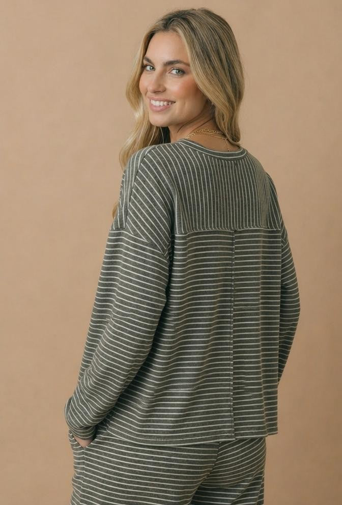 woman wearing a gray and white striped long sleeve top, smiling over her shoulder against a neutral background