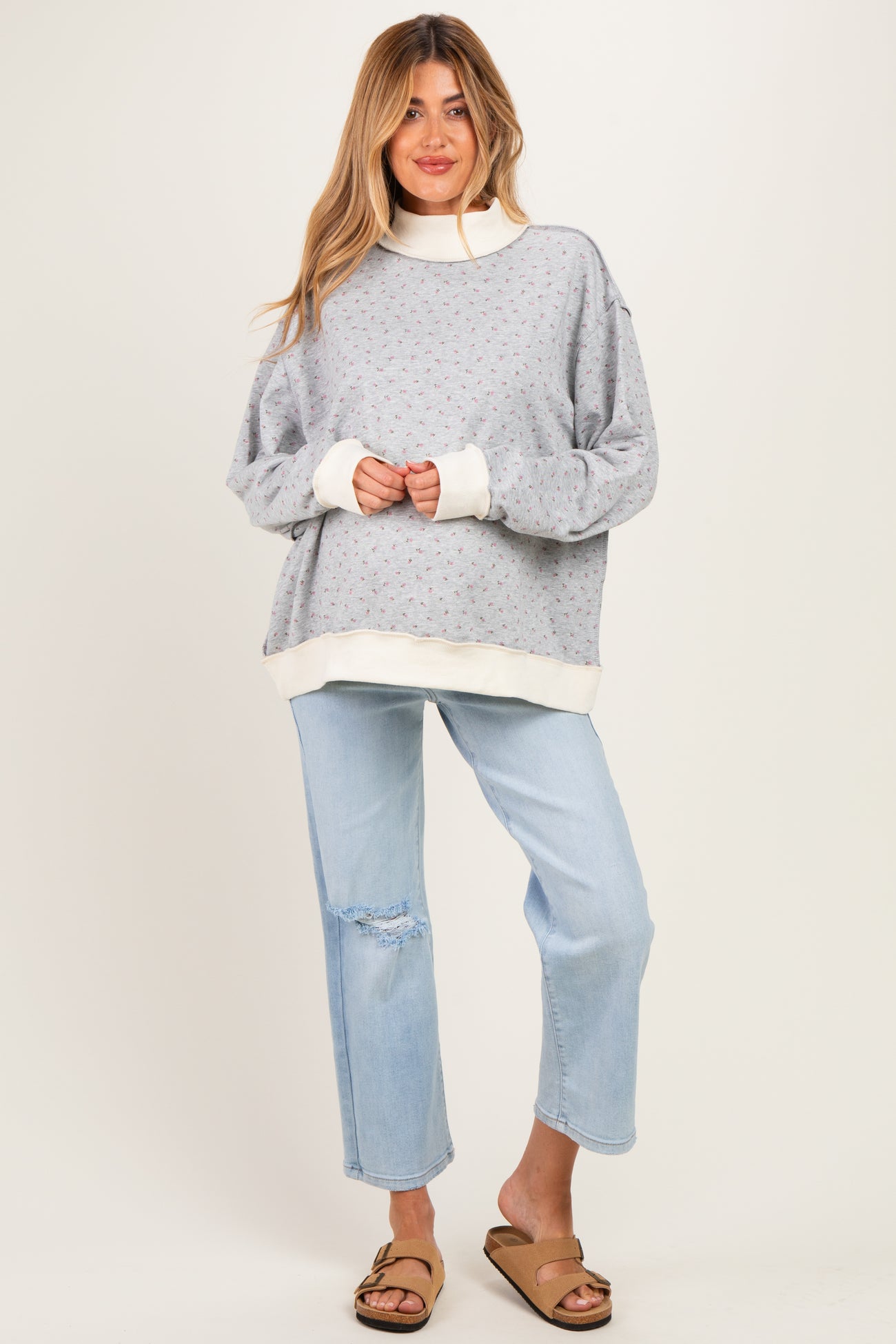 woman wearing a light gray maternity sweatshirt with floral print and white cuffs, paired with light blue distressed jeans