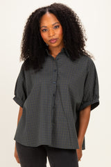 woman wearing a dark green and navy plaid oversized button-up shirt with rolled sleeves