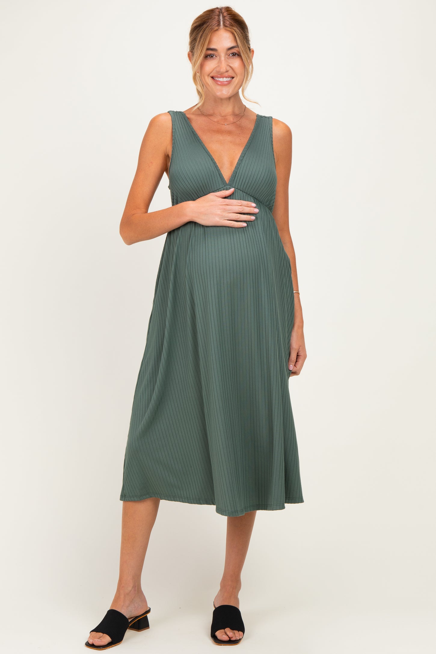 woman wearing a green maternity dress with a plunging neckline and pleated detail, holding her baby bump
