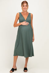 woman wearing a green maternity dress with a plunging neckline and pleated detail, holding her baby bump