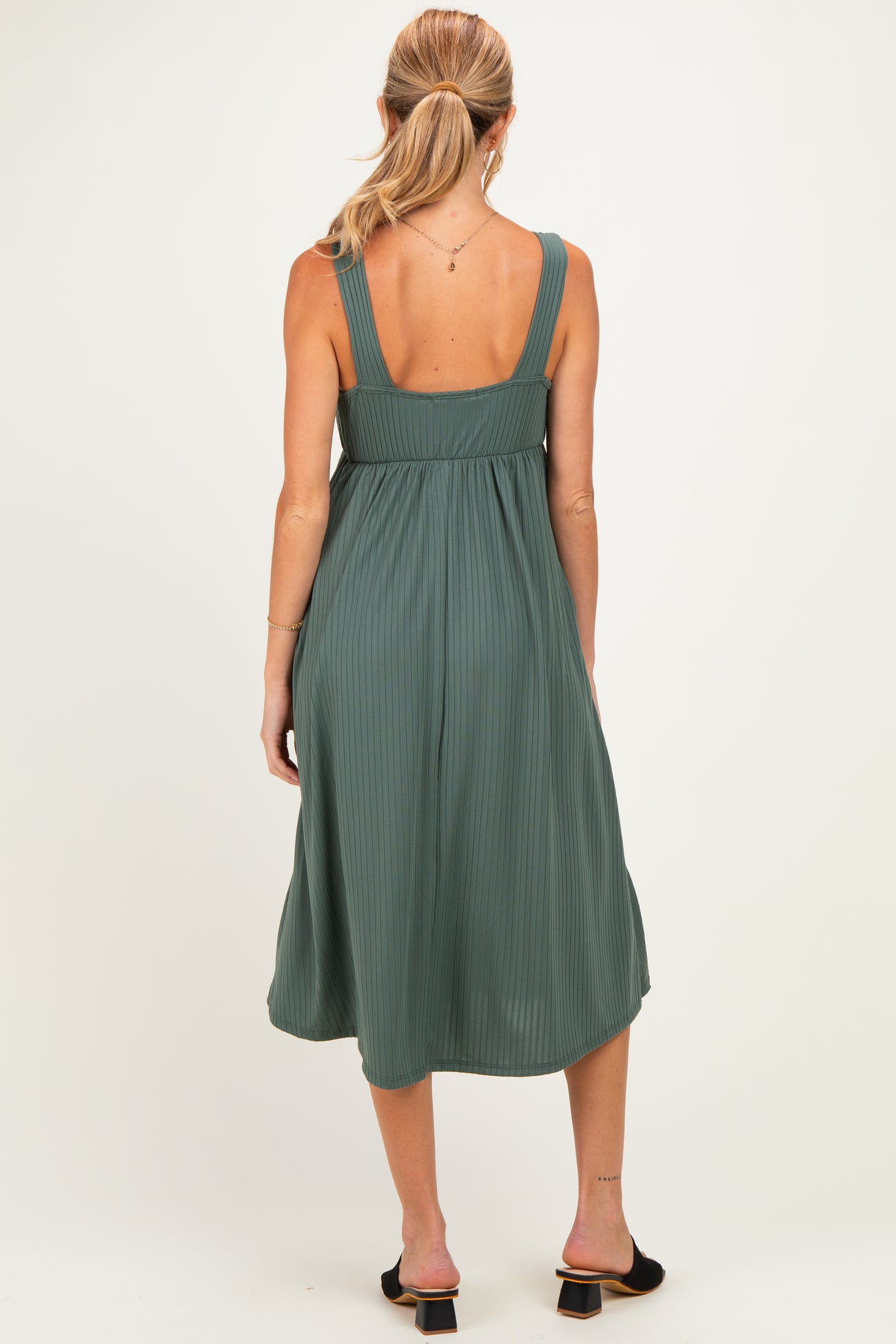 woman wearing a dark green ribbed midi maternity dress, showing a relaxed fit and spaghetti straps from the back
