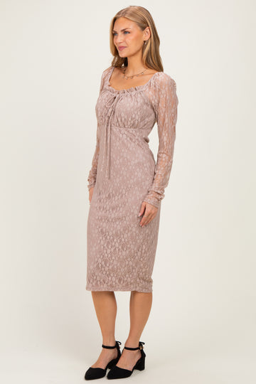 woman wearing a blush pink lace long sleeve midi dress with a tie detail at the neckline and black heels