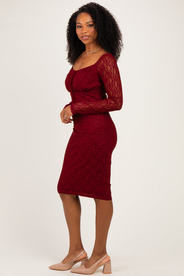woman wearing a burgundy lace long sleeve bodycon dress and nude heels, standing sideways with a slight smile