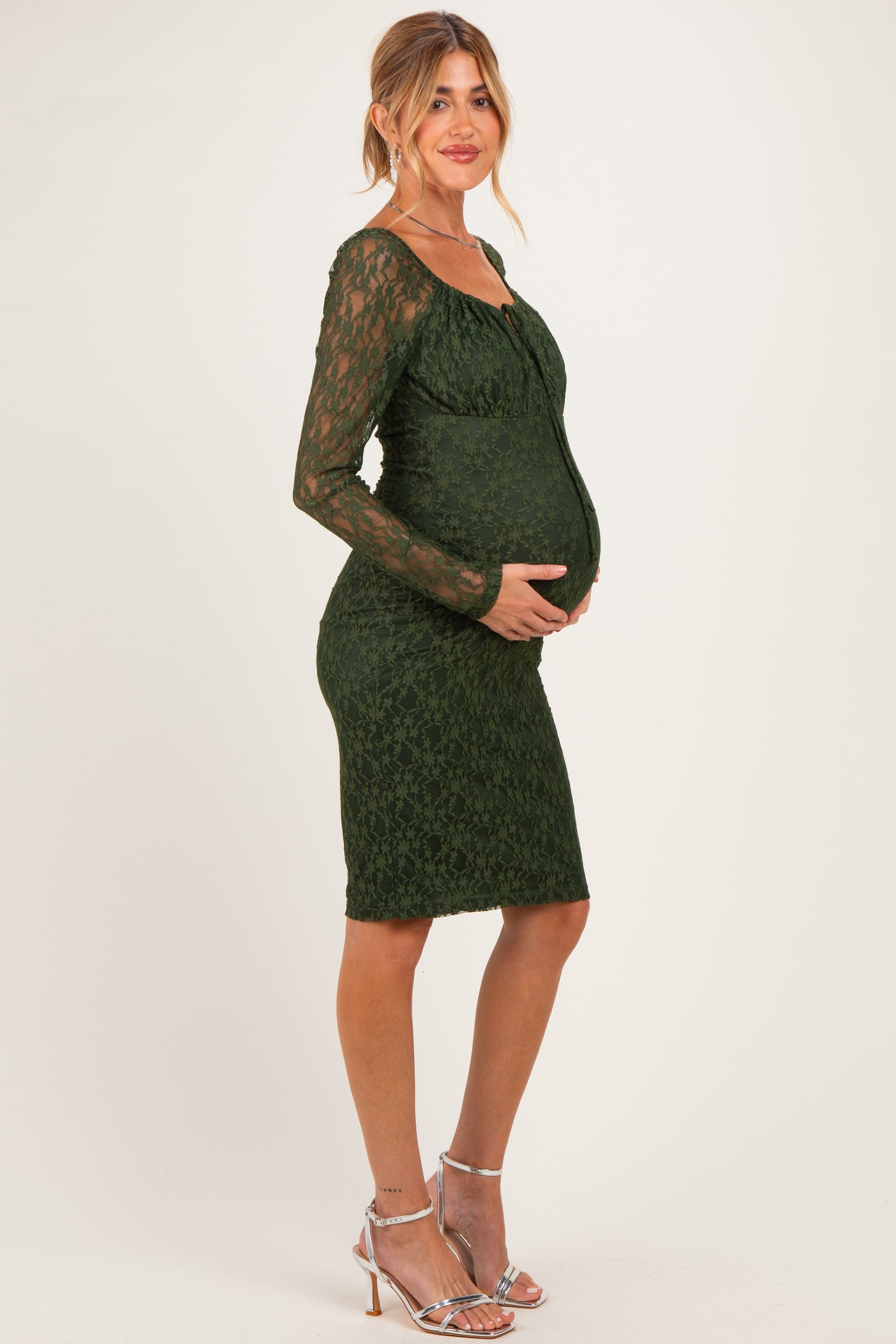 woman wearing a dark green lace maternity dress, fitted style, showing her baby bump with long sleeves and a sweetheart neckline