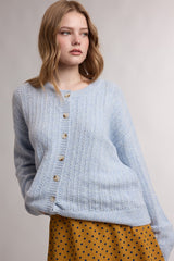 woman wearing a light blue button-up textured cardigan over a yellow polka dot skirt