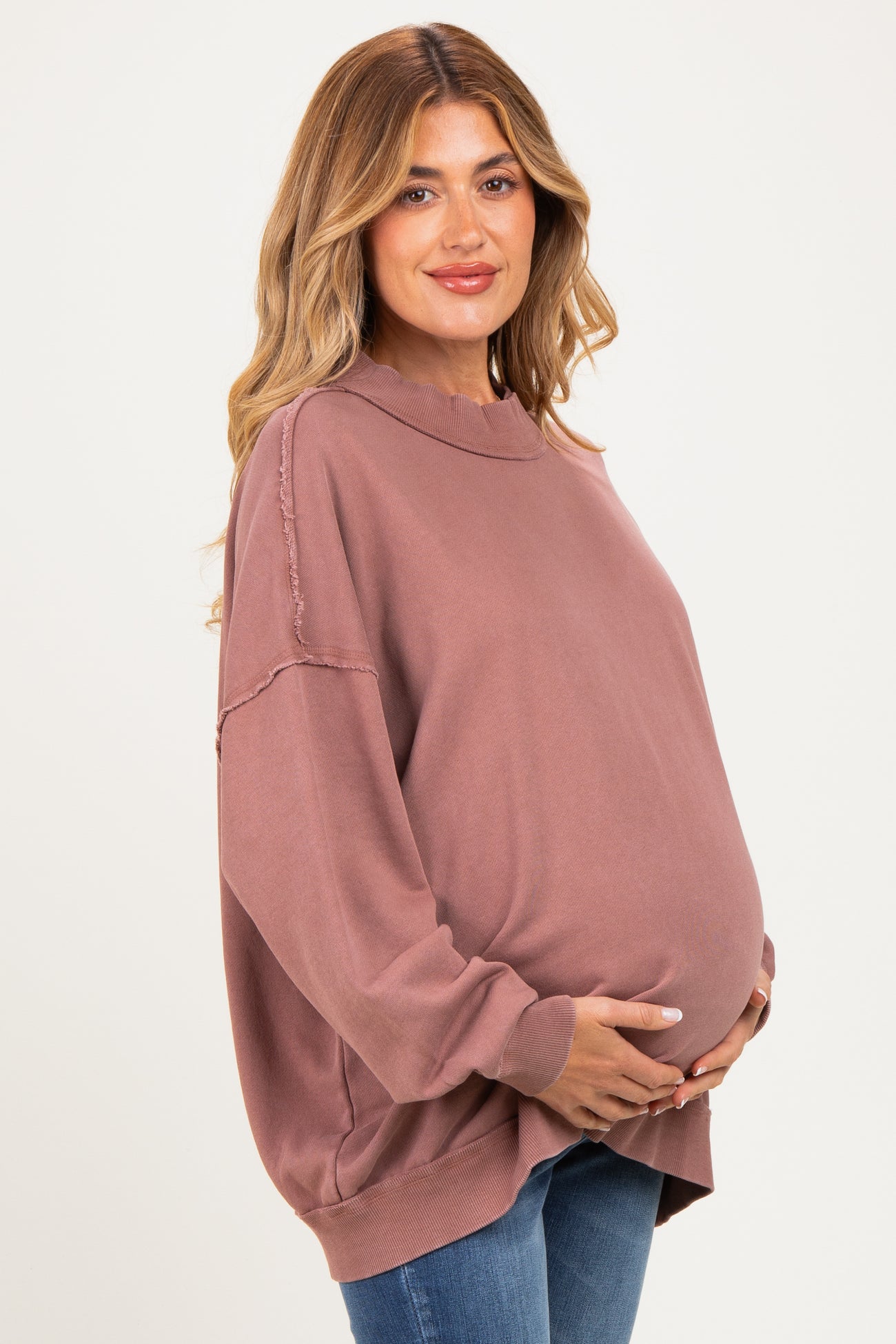 woman wearing a dusty rose oversized maternity sweatshirt and holding her baby bump