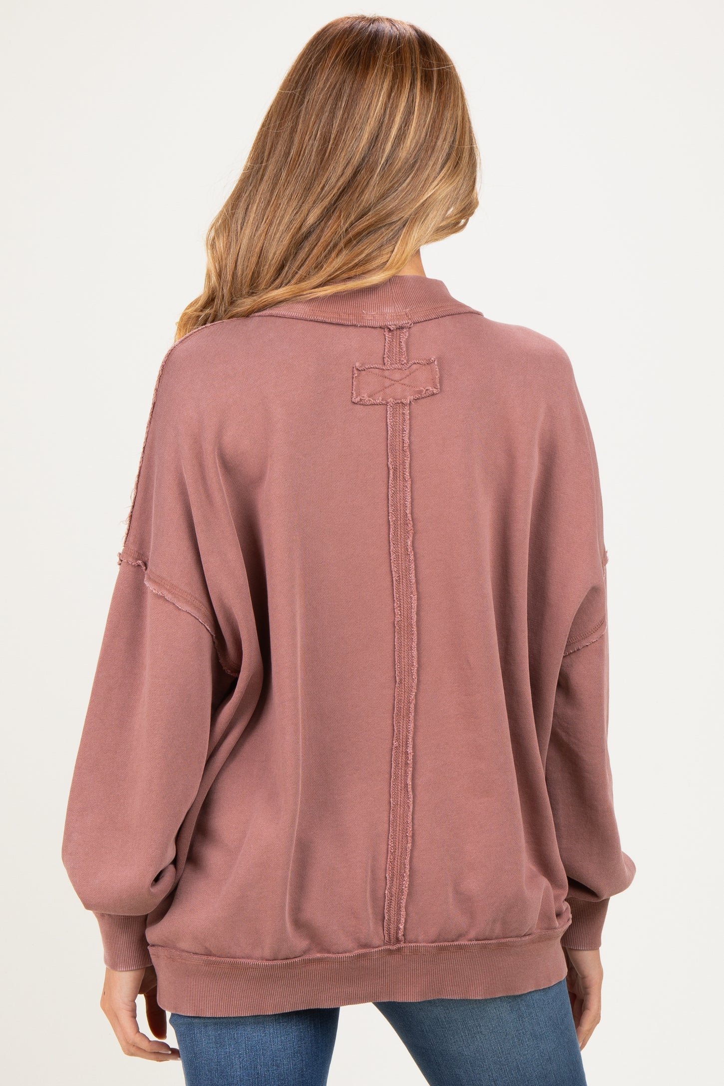 woman wearing a mauve oversized maternity sweatshirt with a relaxed fit and distressed detailing on the back