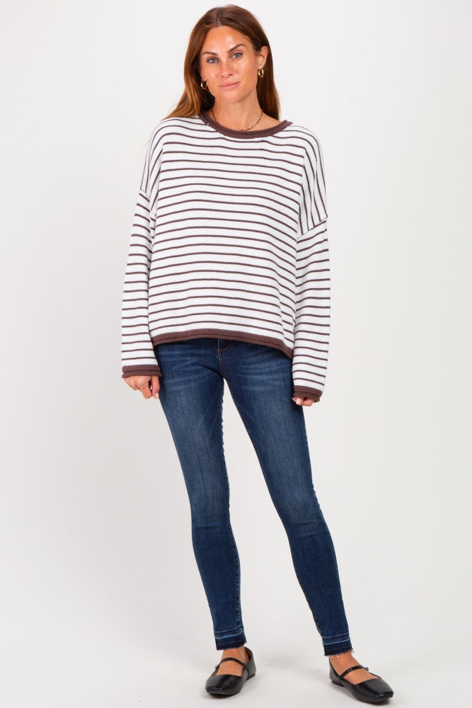 woman wearing a white and brown striped oversized sweater with dark blue skinny jeans and black flats