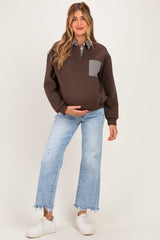 woman wearing a brown maternity sweatshirt with a checked pocket and blue distressed jeans, holding her baby bump