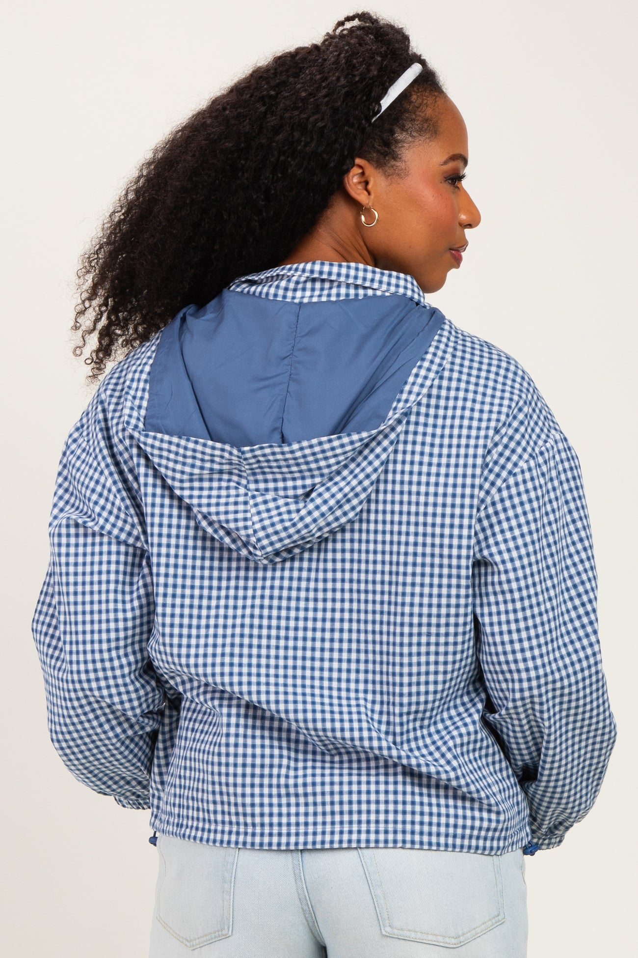 woman wearing a blue and white gingham check hooded jacket, viewed from the back