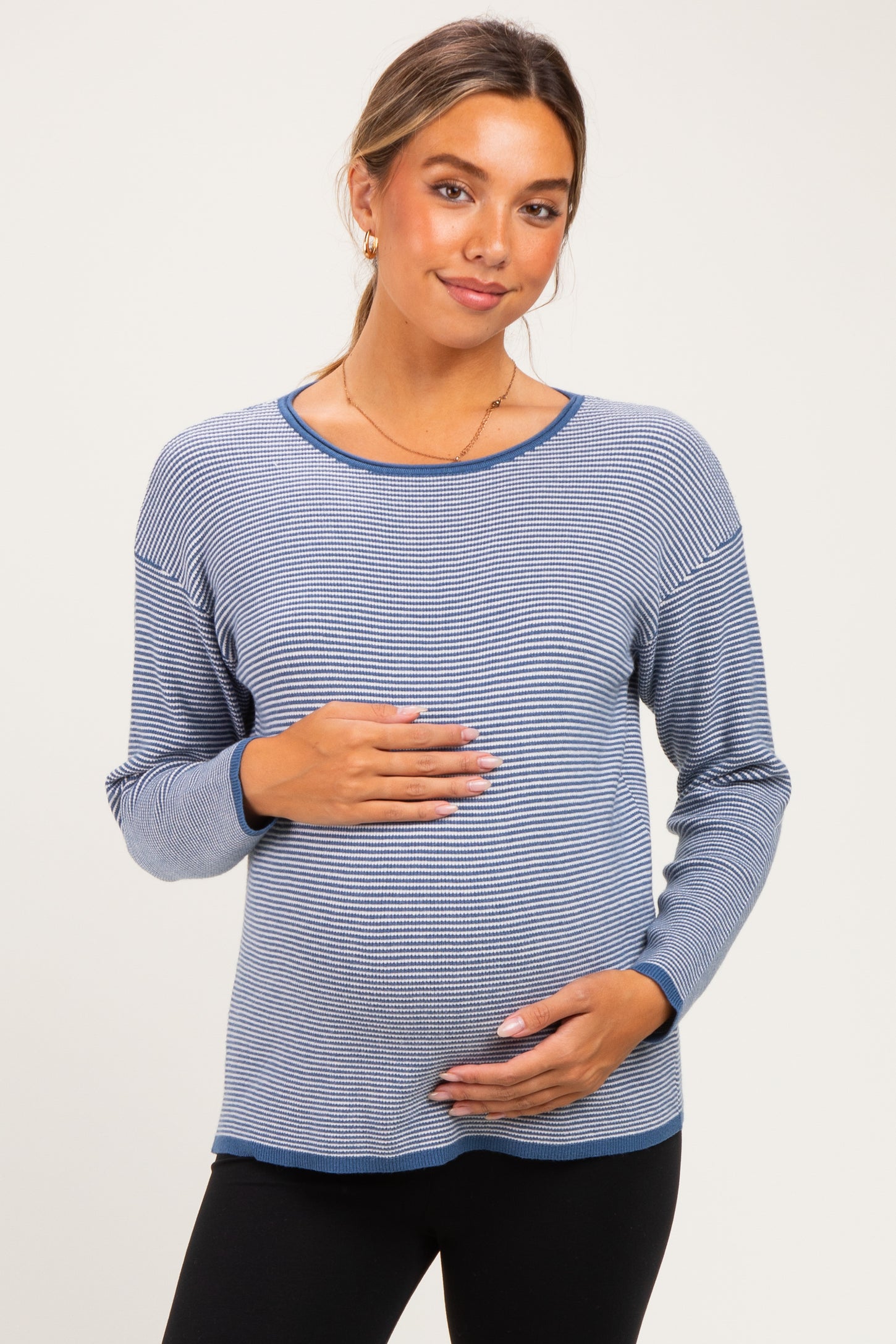 woman wearing a navy and white striped maternity top, gently cradling her baby bump