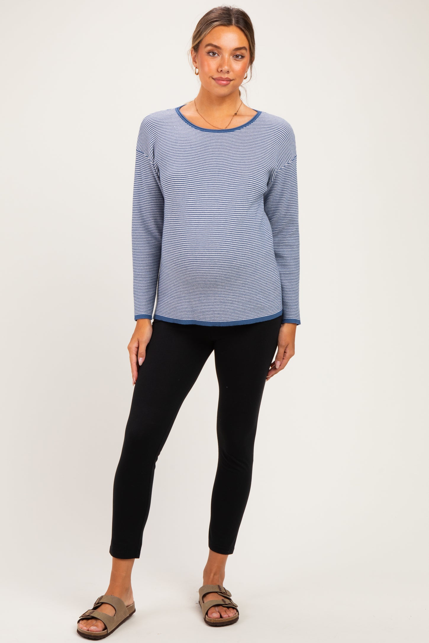 woman wearing a light blue maternity sweater and black leggings with a visible baby bump