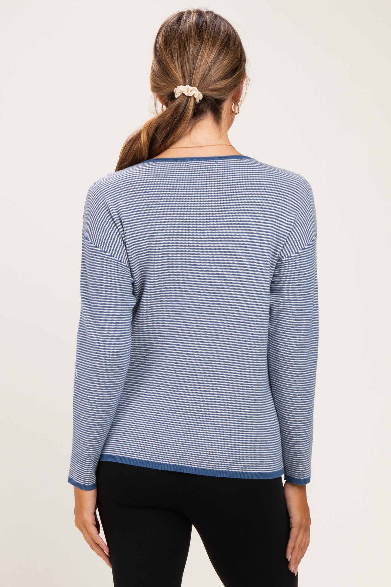 woman wearing a striped blue maternity sweater with long sleeves, view of the back, paired with black leggings