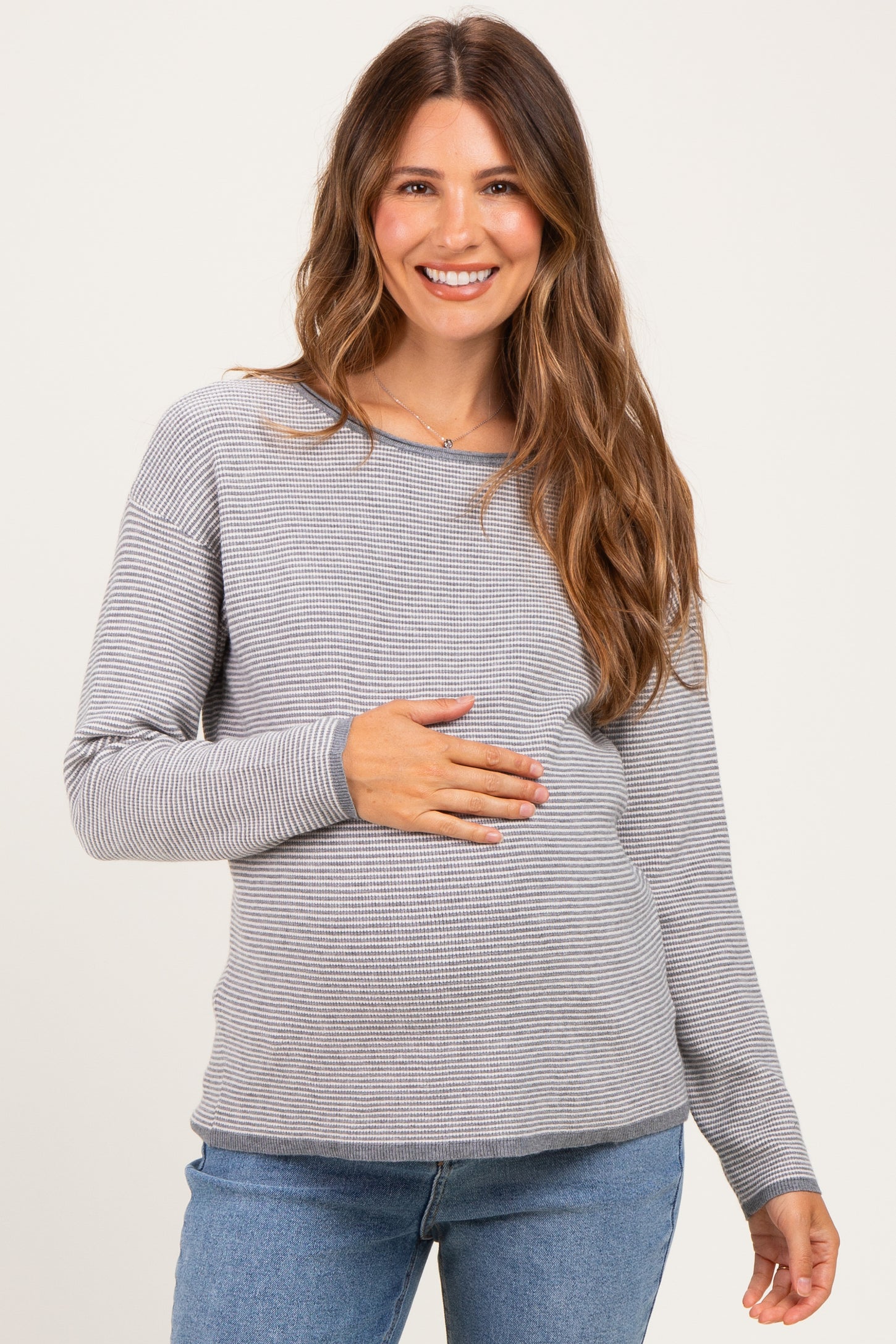 woman wearing a gray and white striped long sleeve maternity top and holding her baby bump