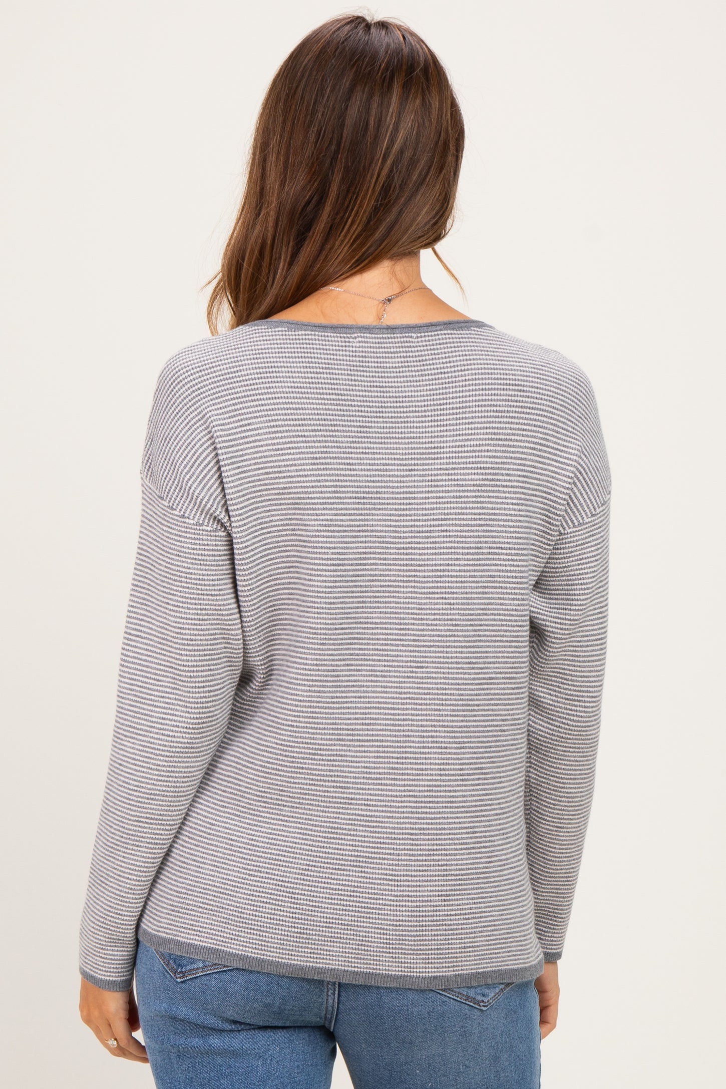 woman wearing a gray striped maternity sweater, shown from the back, paired with blue jeans