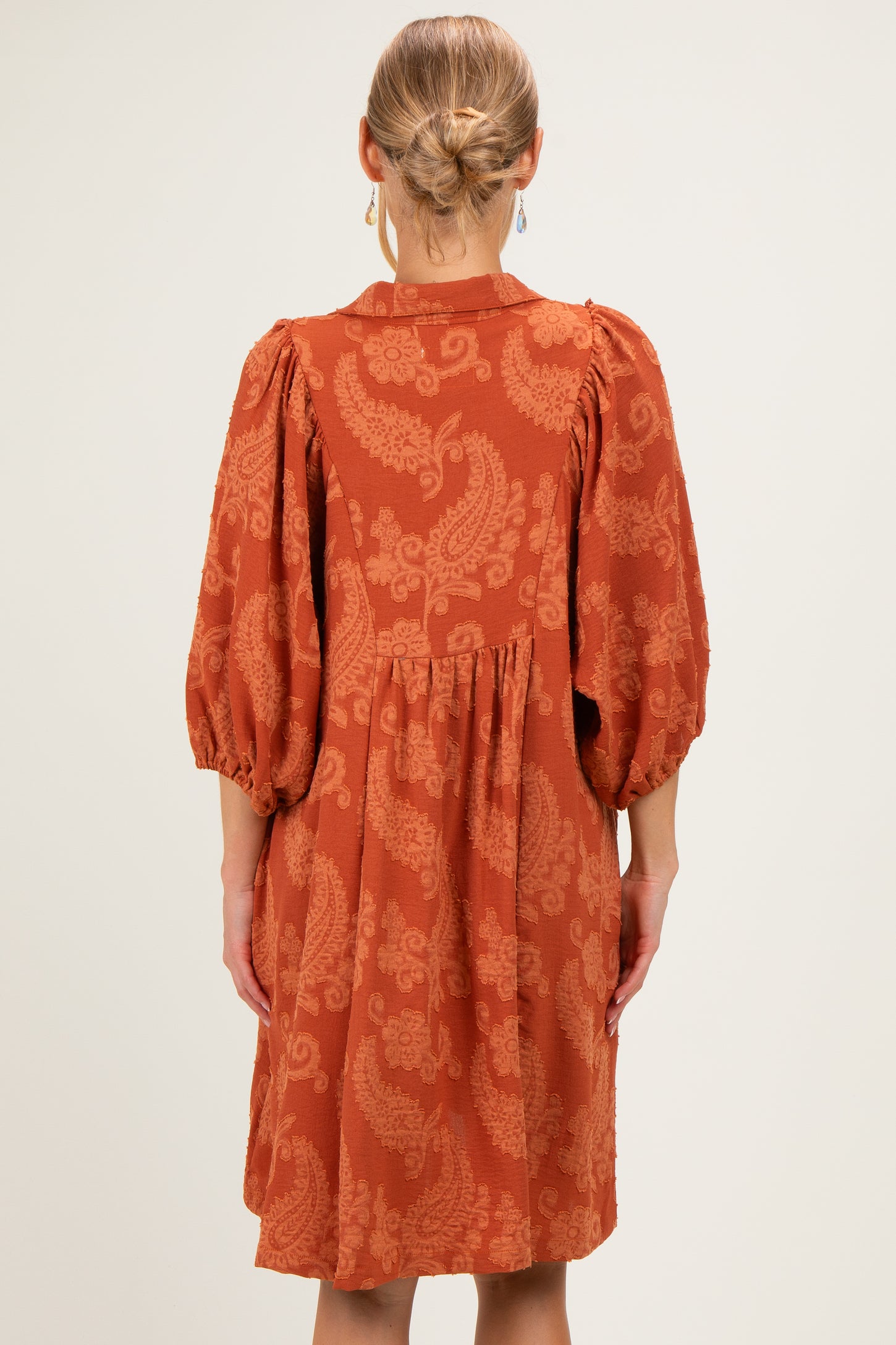 woman wearing an orange patterned short sleeve dress with a tiered skirt and puff sleeves, shown from the back
