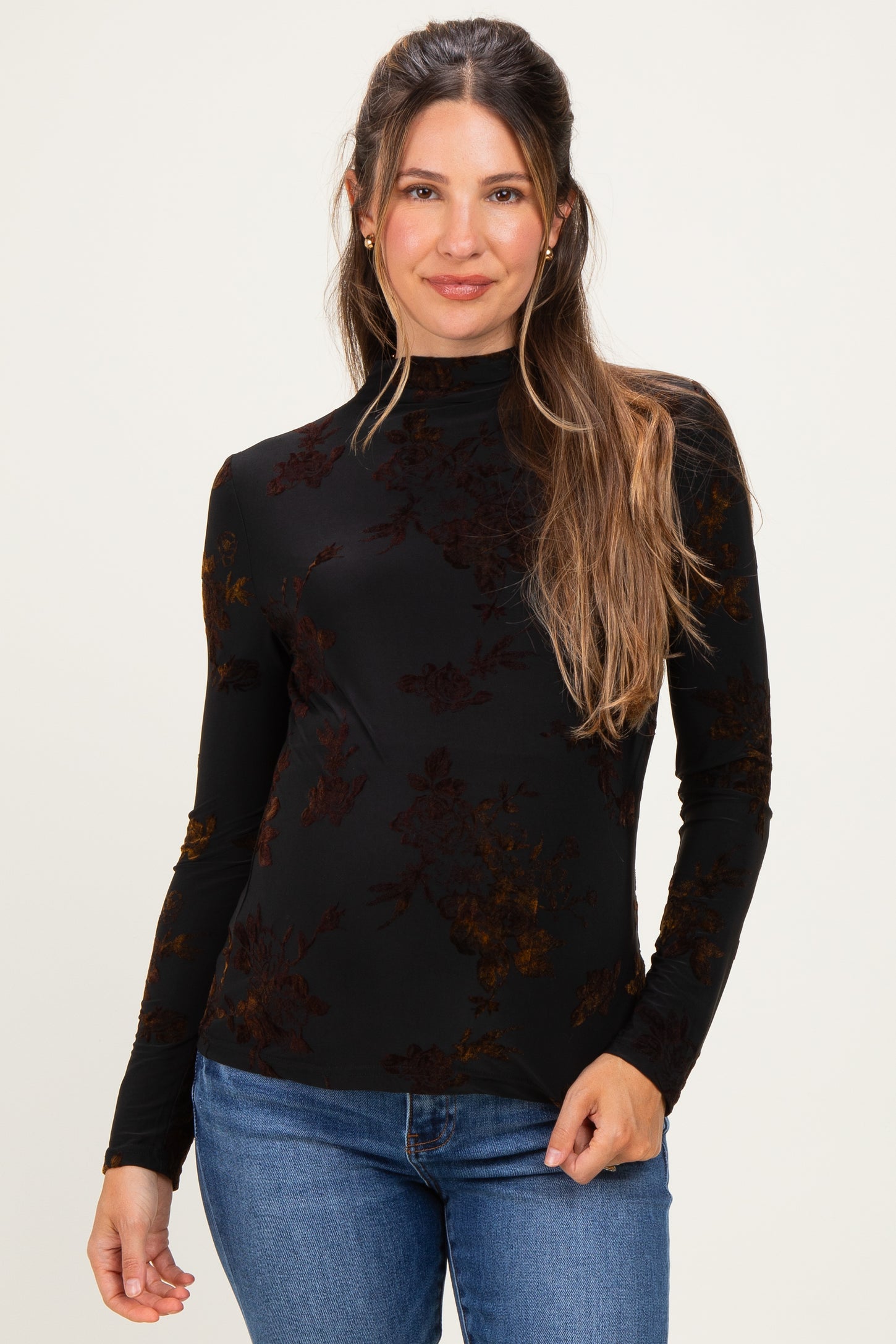 woman wearing a black floral long sleeve maternity top with a high neckline and holding her baby bump